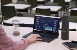 Close-up of a hand on a laptop keyboard, with financial charts and graphs visible on the screen. An hourglass nearby symbolises time-sensitive authorisation, highlighting the importance of timeliness in streamlining financial processes.