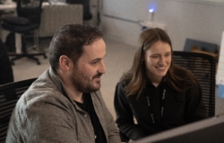 Two colleagues collaborating at a computer in a modern office setting, smiling as they review information on the screen.