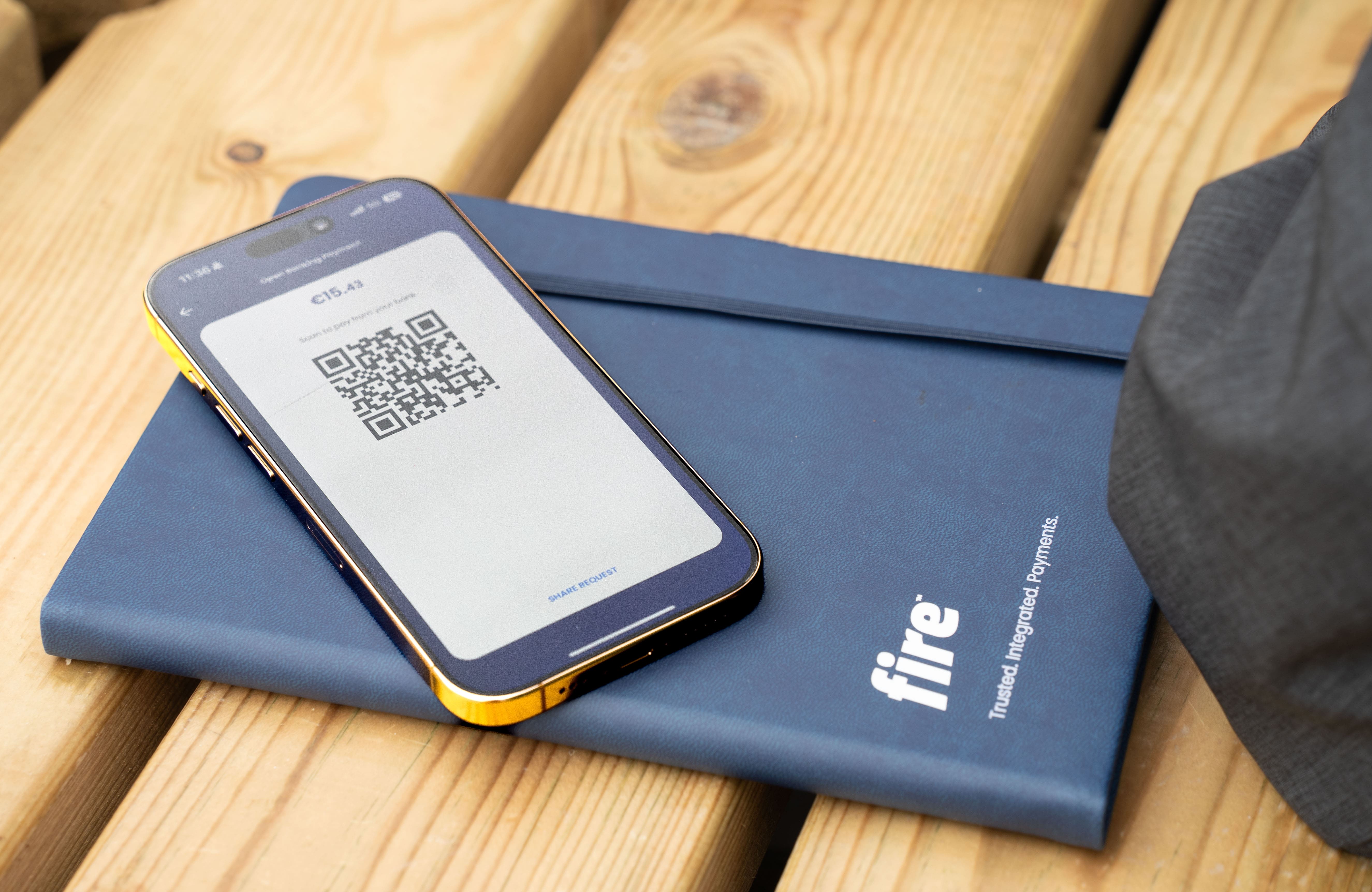 Smartphone displaying an open banking and QR code in the Fire mobile application, above a dark blue notebook with the Fire logo.