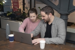 Two people looking at a laptop screen, reviewing information together. One person is explaining something on the screen to the other, representing collaboration and illustrating how multiple individuals within a business can have varying levels of access and control over payments and accounts.